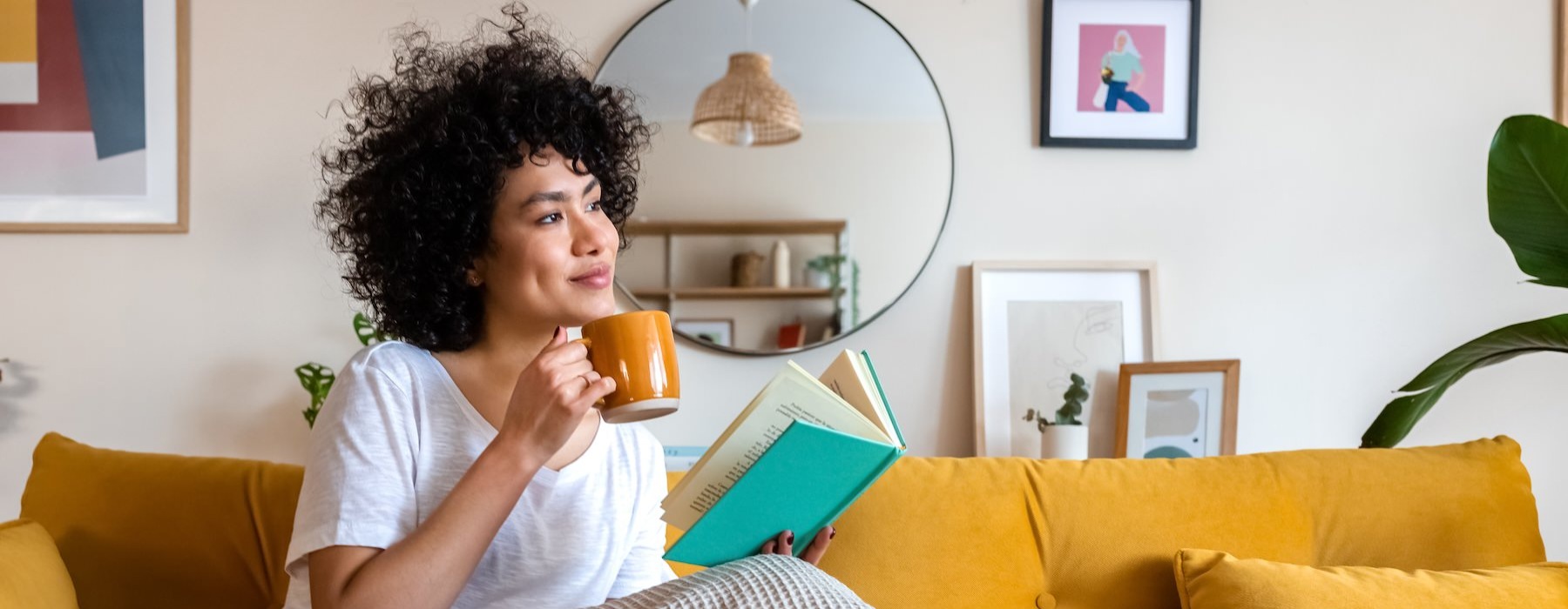 a woman sitting on a couch reading a book with a mug in her hand