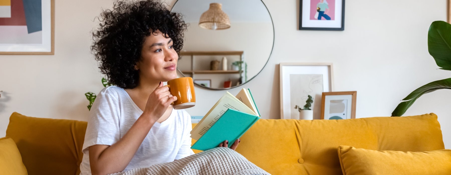 a woman sitting on a couch reading a book with a mug in her hand
