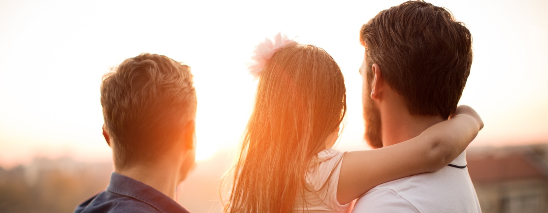 two men holding a little girl watching the sun set
